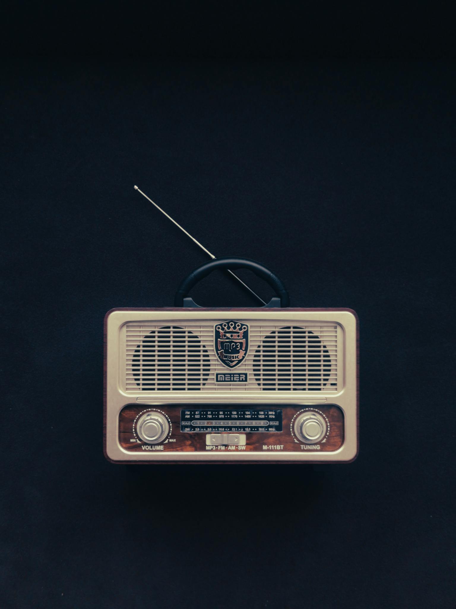 Classic vintage radio with knobs and antenna against a black background, showcasing retro technology.